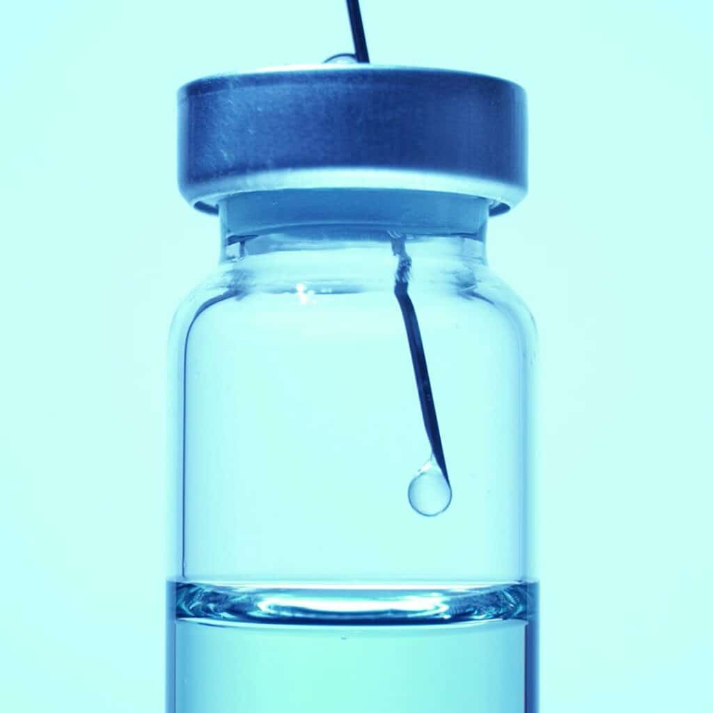 Picture of a flask with a syringe inside of it dropping some liquid. Toxins in injectable products. Toxins in parenteral product packaging.