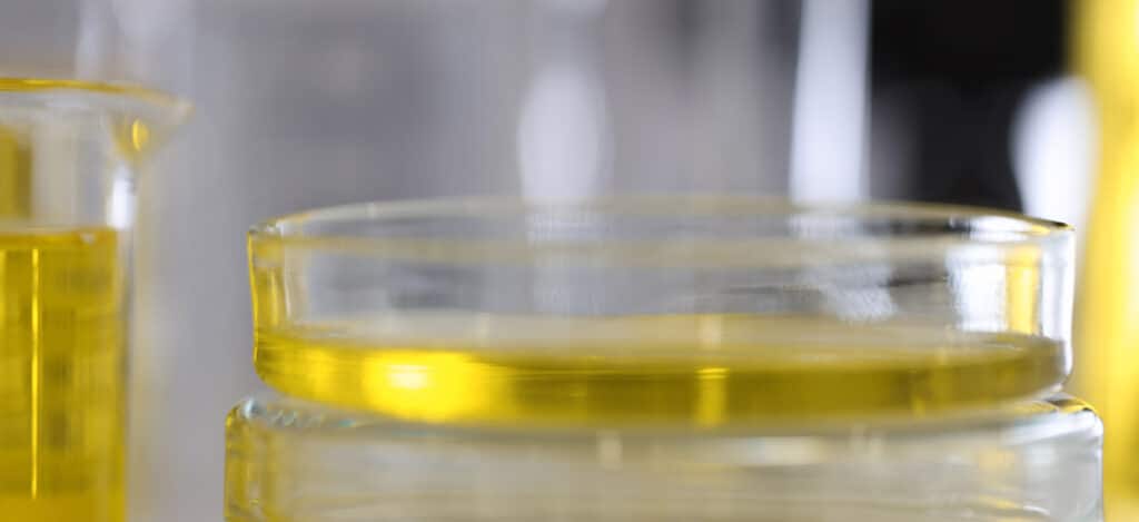 Close picture of a dropper dropping yellow liquid on a petri plaque. Preservative efficacy testing vs stability testing. Preservative challenge testing vs stability testing. Differences between preservative efficacy testing and stability testing. What products need preservative efficacy testing. What products need stability testing. Stability testing for cosmetic products and parenteral products