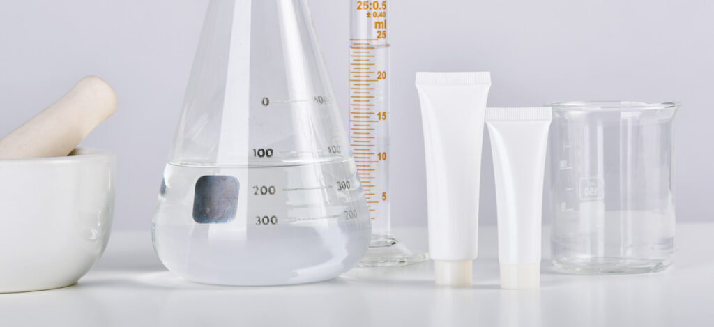 Picture of flasks, test tubes, and a bowl filled with cosmetic products on a laboratory table. Fill requirements for cosmetic products. Minimum fill requirements for cosmetics. What are cosmetic products. Why are minimum fill requirements necessary. Necessary fill requirements for cosmetics. Cosmetic products fill requirements. Acceptance criteria for cosmetic formulations