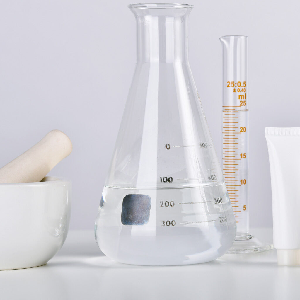 Picture of flasks, test tubes, and a bowl filled with cosmetic products on a laboratory table. Fill requirements for cosmetic products. Minimum fill requirements for cosmetics. What are cosmetic products. Why are minimum fill requirements necessary. Necessary fill requirements for cosmetics. Cosmetic products fill requirements. Acceptance criteria for cosmetic formulations